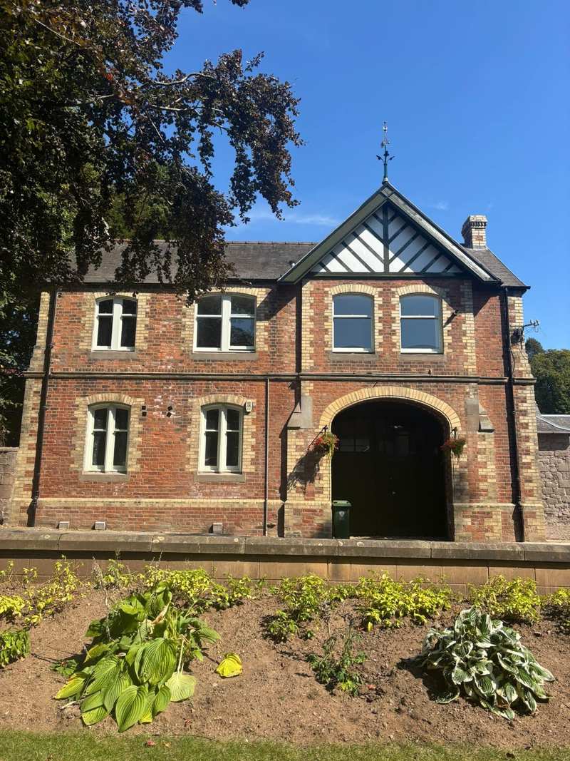 Red brick and sandstone coach house with a decorative timber gable, arched carriage doors and sash windows