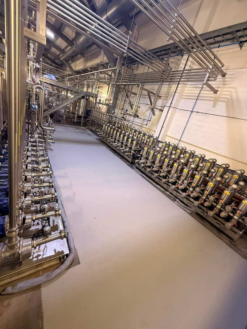 Cream resin floor in an aisle between stainless pipework and a row of valves