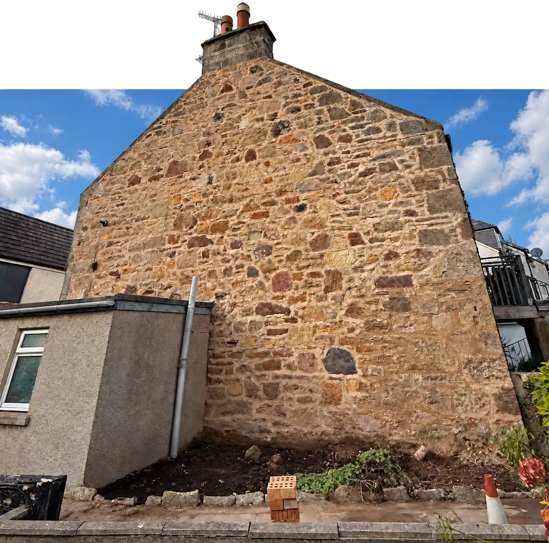 Restored rubble stone gable end with its chimney stack rising above the frame, after lime repointing